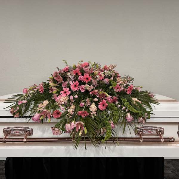 Pink floral spray arranged on top of a white casket