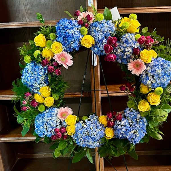 Circular floral wreath with blue hydrangeas, yellow roses, and pink daisies
