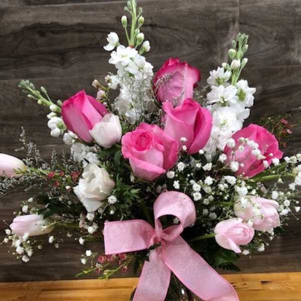 Pink and white rose bouquet in a glass vase with a pink ribbon