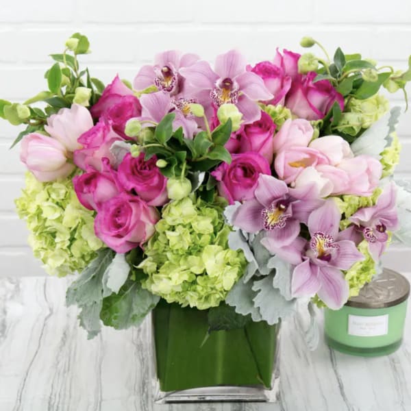Pink roses and orchids arranged in a green vase with lime hydrangeas