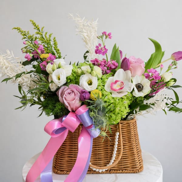 Mixed pink and white flowers in a wicker basket with ribbon