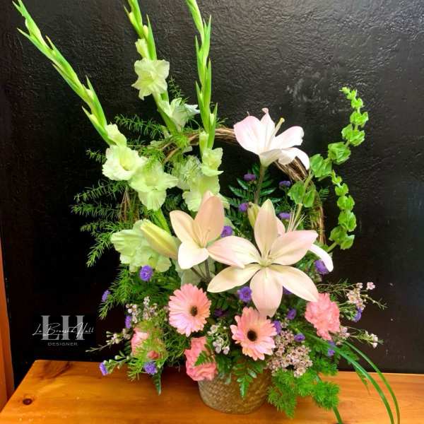 Pastel floral arrangement with lilies, gerbera daisies, and gladiolus in a woven basket