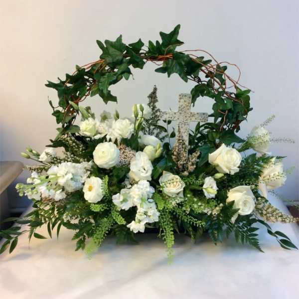 White floral arrangement with a decorative cross and ivy arch