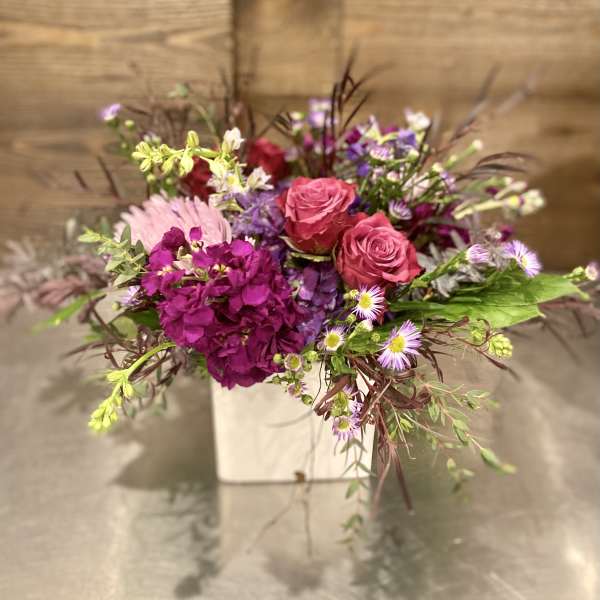 Pink roses and purple flowers arranged in a white box
