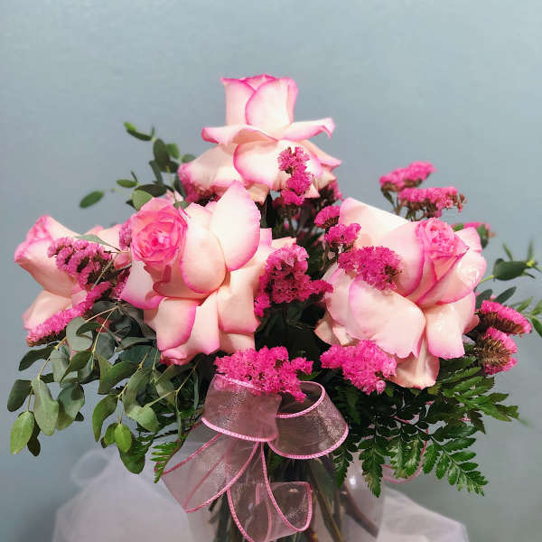 Pink-tipped white roses with bright pink filler flowers in a clear glass vase with a pink ribbon.