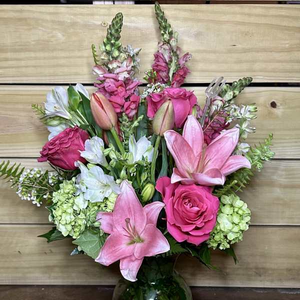 Pink lilies and roses arranged in a glass vase with white blooms