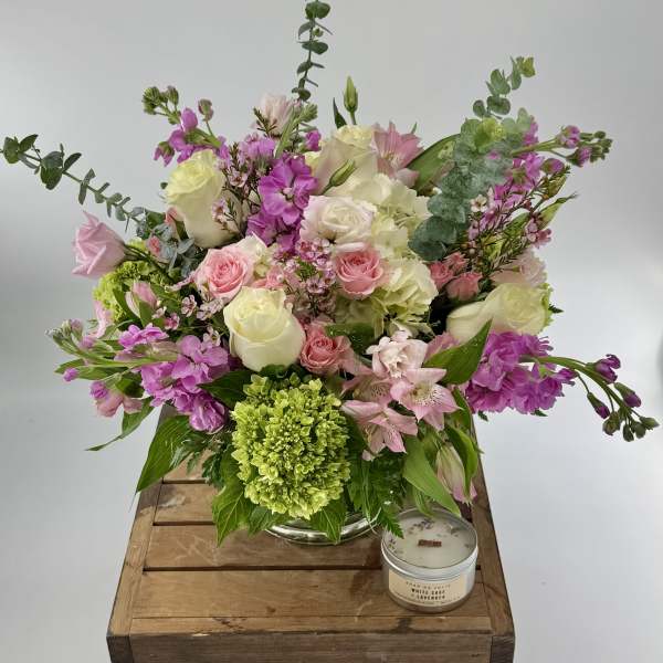 Pink and white mixed flower arrangement in a glass vase with a green bloom and a small candle beside it