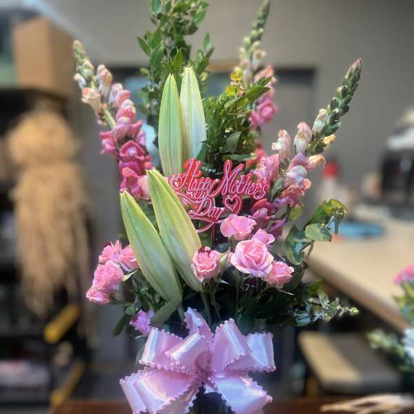 Pink roses and lilies in a glass vase with a pink ribbon and Mother's Day pick