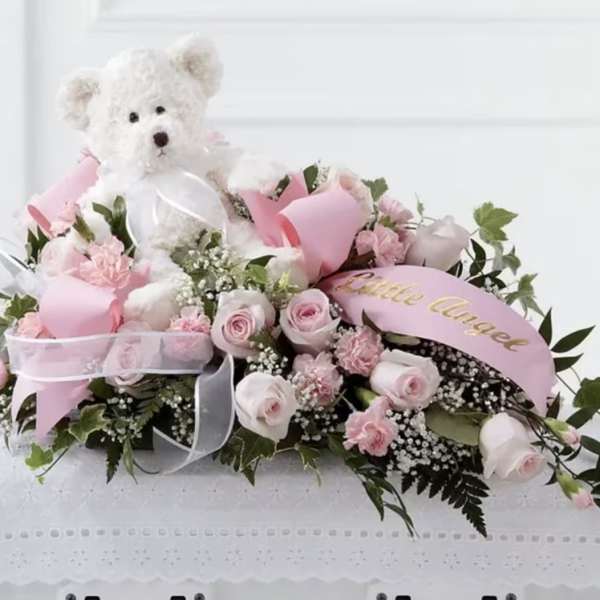 Pink rose arrangement with a white teddy bear and ribbon accents