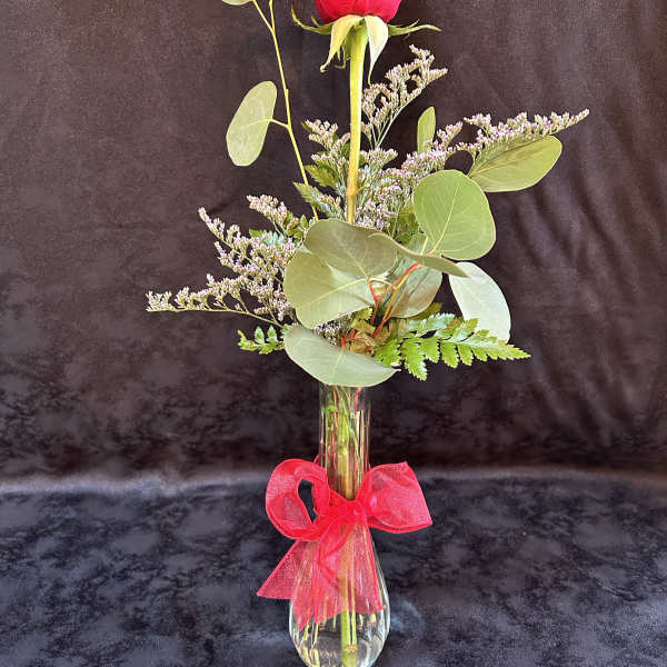 Single red rose in a clear vase with a pink ribbon