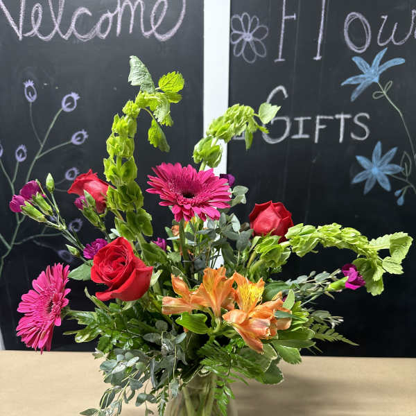 Mixed bouquet with roses, gerbera daisies, and orange alstroemeria in a glass vase