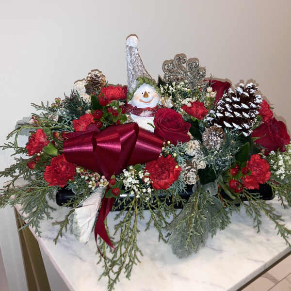 Christmas floral centerpiece with red flowers, pinecones, and a snowman ornament