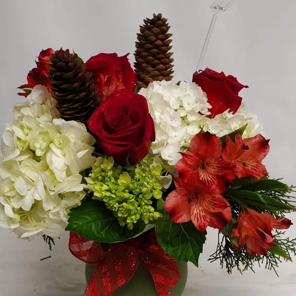 Red roses and white hydrangeas in a green vase with pinecones and a red ribbon