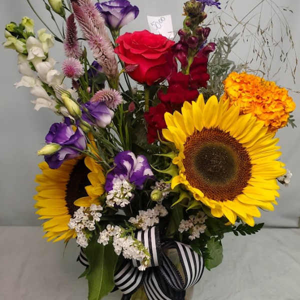 Mixed bouquet with sunflowers, roses, and purple blooms in a glass vase