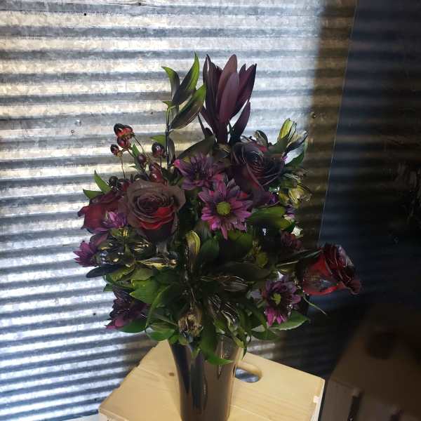 Dark purple bouquet in a black vase with roses and daisy-like blooms