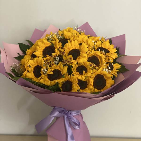 Bouquet of yellow sunflowers wrapped in pink paper with a lavender ribbon