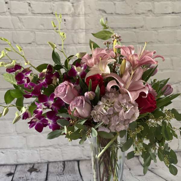 Pink lilies and roses in a clear glass vase with purple orchids