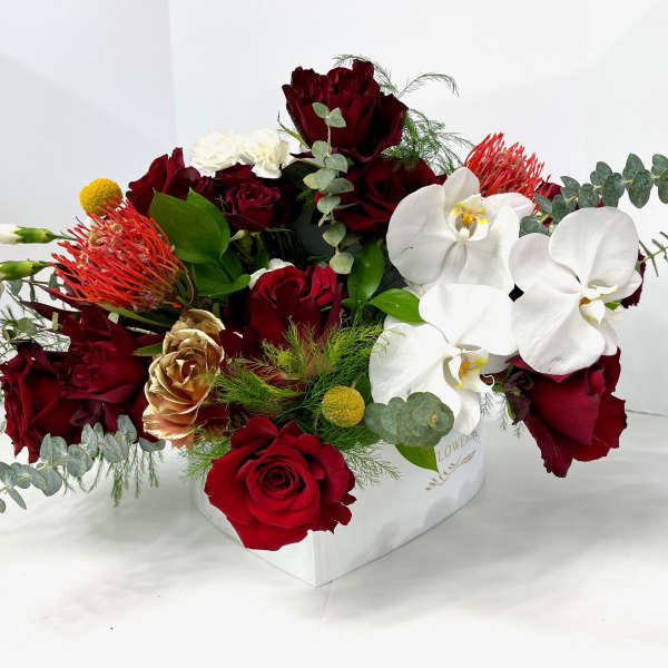 Red roses and white orchids arranged in a white box