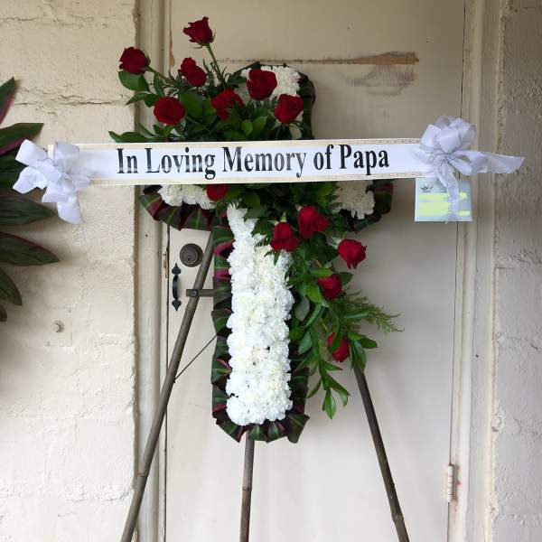 Standing memorial cross of red roses and white flowers with a ribbon banner