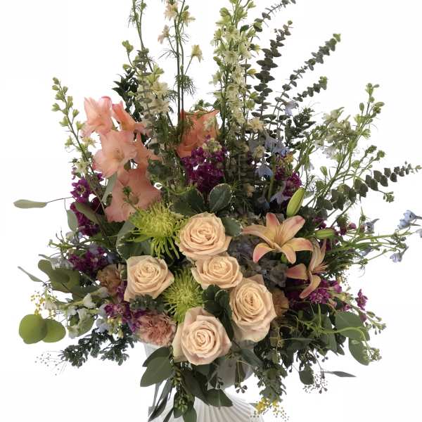 Tall mixed floral arrangement with peach roses and lilies in a white vase