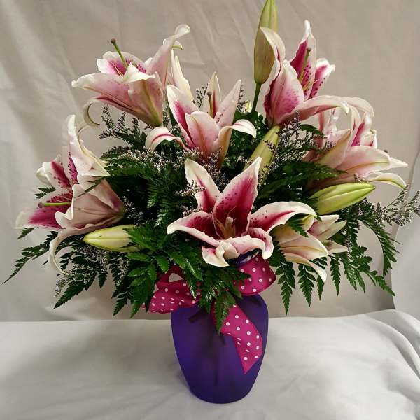 Pink and white lilies arranged in a purple vase with a polka-dot ribbon