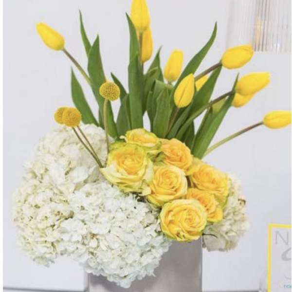 Yellow tulips and roses arranged with white hydrangeas in a silver vase