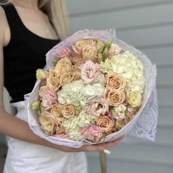 Handheld bouquet of blush roses and pale hydrangeas wrapped in lavender paper