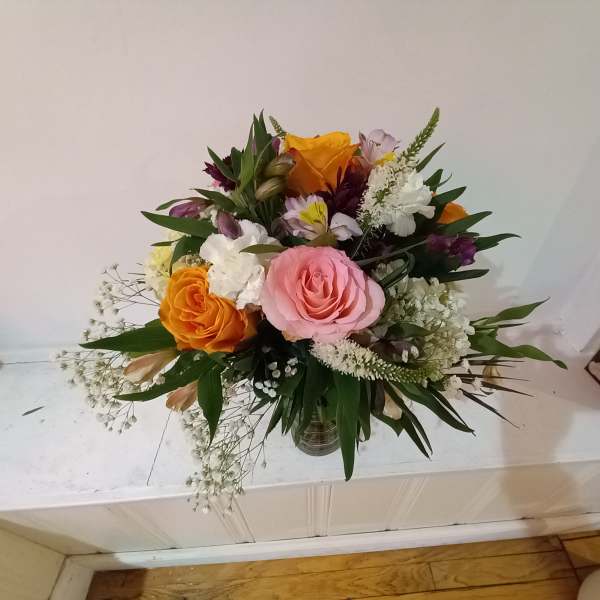 Mixed bouquet of pink and orange roses with white filler flowers in a glass vase