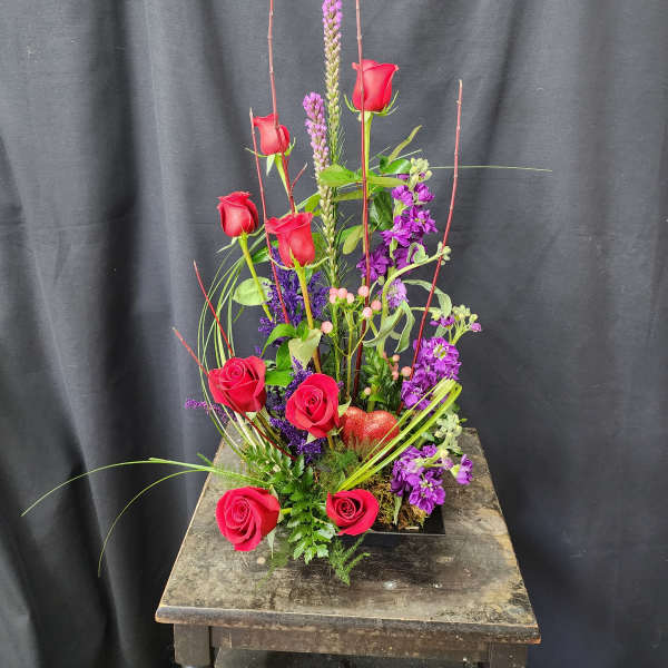 Tall arrangement of red roses and purple flowers in a low black container
