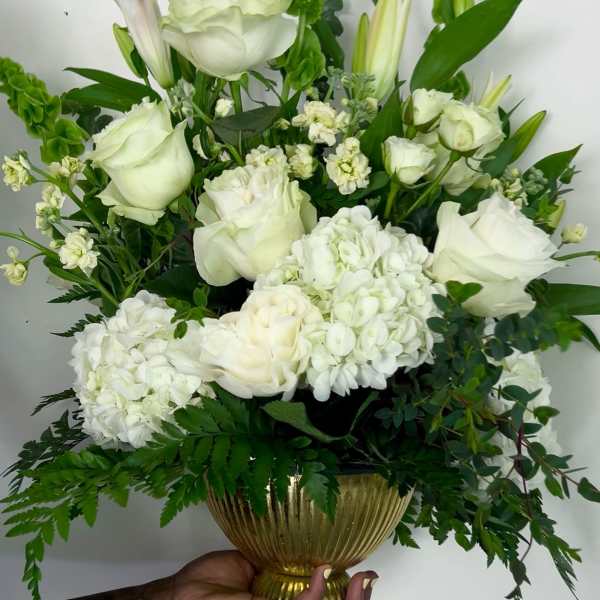 White floral arrangement in a gold vase with lilies and roses