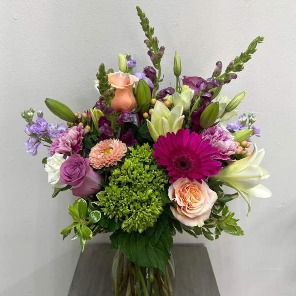 Mixed bouquet in a glass vase with roses, lilies, and purple blooms
