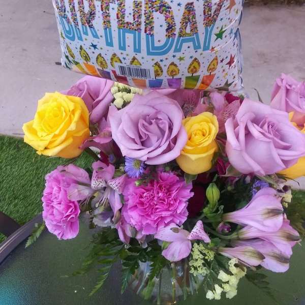 Birthday balloon above a bouquet of roses and pink flowers in a glass vase