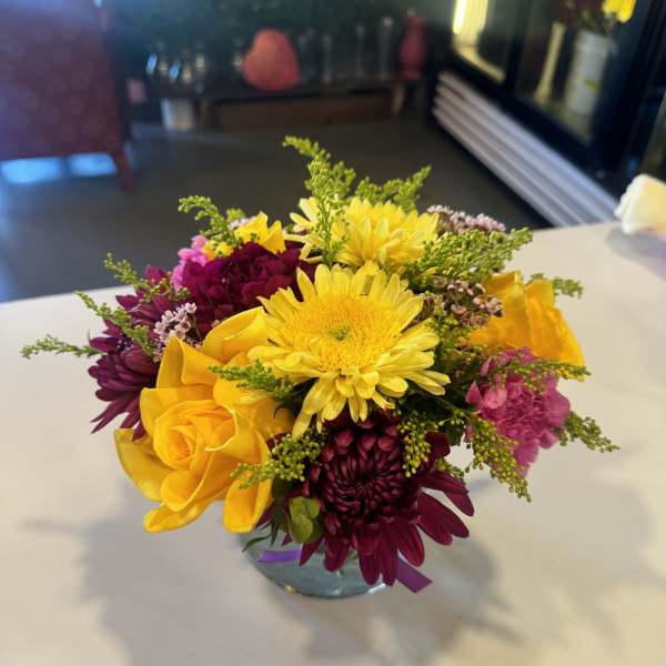 Mixed bouquet of yellow, pink, and purple flowers in a glass vase