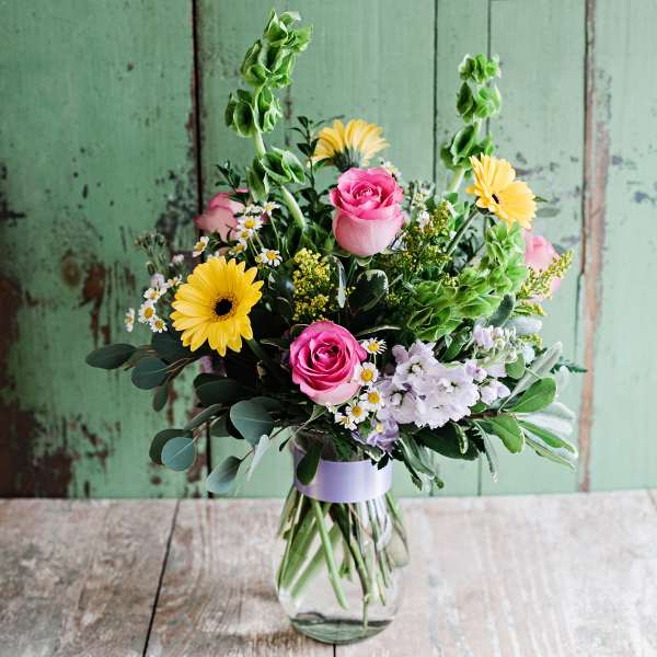 Mixed bouquet of pink roses, yellow daisies, and white flowers in a glass vase