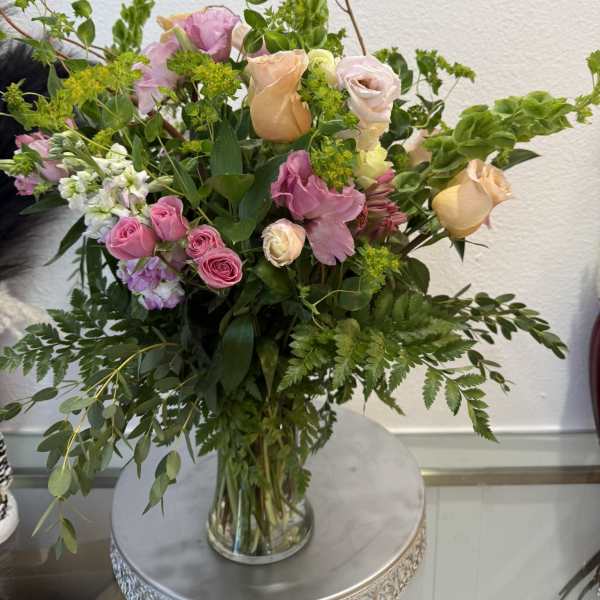 Mixed pink and peach roses in a clear glass vase with greenery