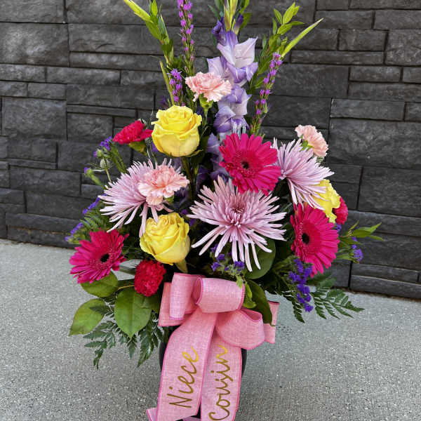 Colorful standing floral arrangement with pink ribbon in a black container