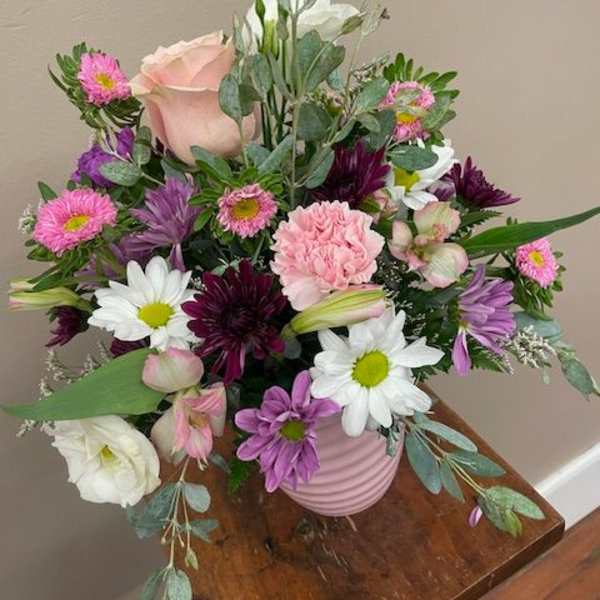 Mixed bouquet of pink, purple, and white flowers in a pink vase