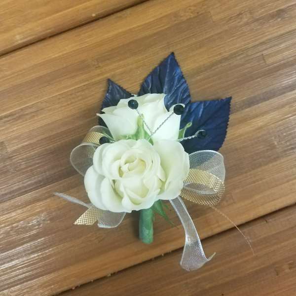 Small white rose corsage with dark blue leaves and ribbon on a wooden surface