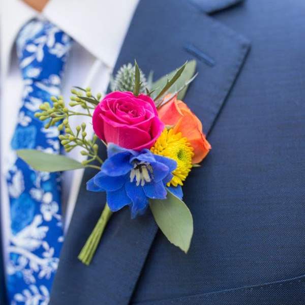 Colorful boutonniere with roses and a blue flower on a suit lapel