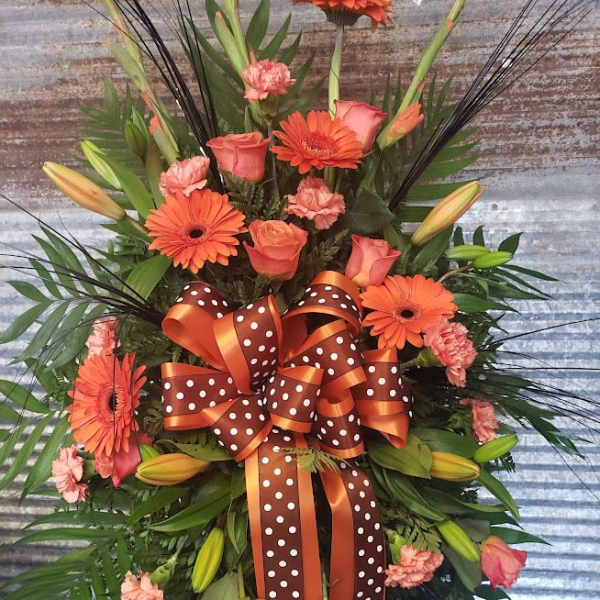 Orange gerbera daisies and roses in a large ribboned floral spray