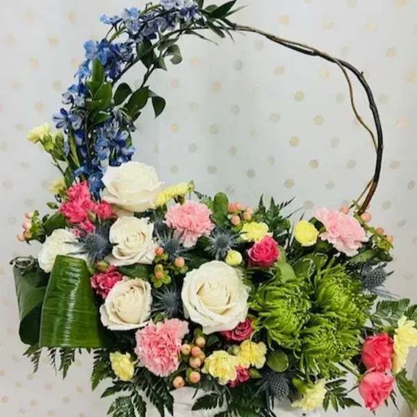 Basket arrangement of mixed flowers with a curved handle and blue blooms