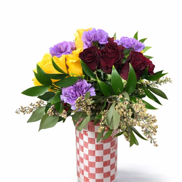 Bouquet of yellow and burgundy roses with purple carnations in a checkered vase