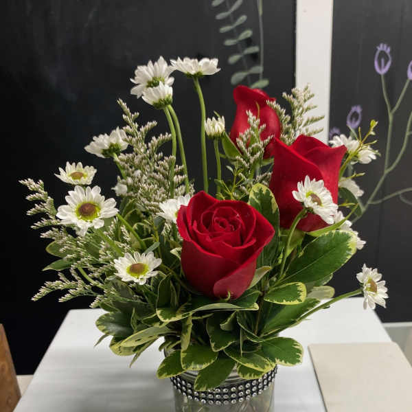 Red roses and white daisies in a glass jar with greenery