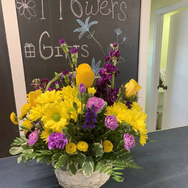 Basket arrangement of yellow daisies, purple flowers, and yellow roses