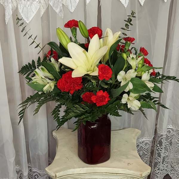 Red carnations and white lilies in a burgundy vase
