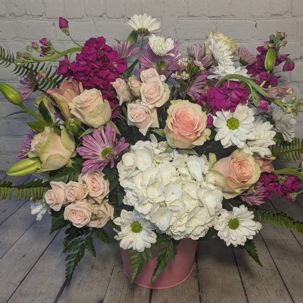 Mixed bouquet of roses, hydrangea, and daisies in a pink container