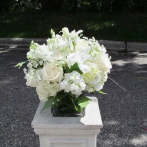 White floral arrangement in a square vase on a pedestal