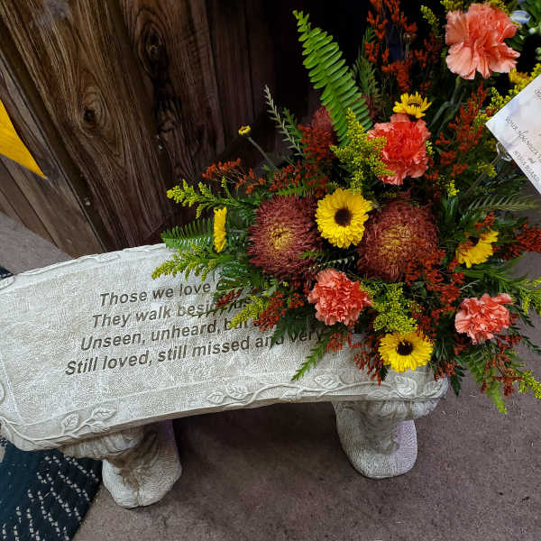 Sympathy spray with yellow daisies and peach carnations on a memorial bench