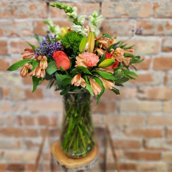 Mixed bouquet in a glass vase with coral, peach, purple, and white blooms