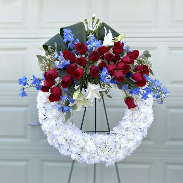 Red roses, blue flowers, and white lilies in a white chrysanthemum wreath